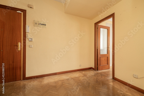 Empty room with entrance door and access door to another room and herringbone oak parquet floors