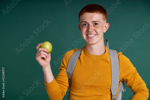 Caucasian teenage boy of red hair holding a green apple in raised hand © gpointstudio