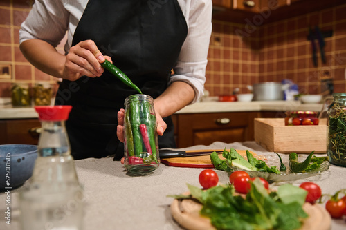 Foto Cropped view of a housewife in a black kitchen apron, filling sterilized glass j