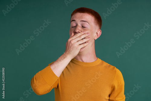 Caucasian teenage boy with red hair with yawing on green background
