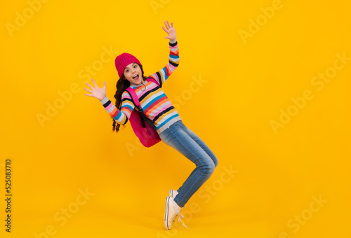 Winter school holiday. Back to school. Teenager schoolgirl with warm hat and sweater on yellow isolated studio background. Winter school. Happy teenager, positive and smiling school girl.