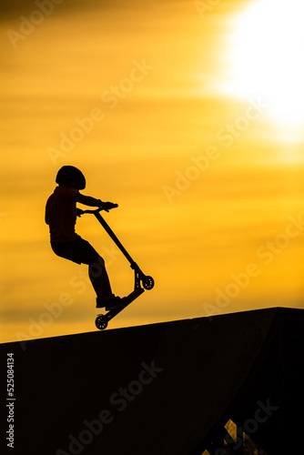 Silhouette of a young  boy riding a scooter against the background of a sea sunset