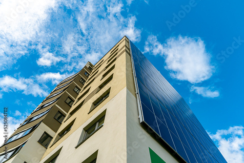 A modern energy-efficient building against the background of clouds. Multi-storey residential building with solar panels on the wall. Renewable energy sources in the city