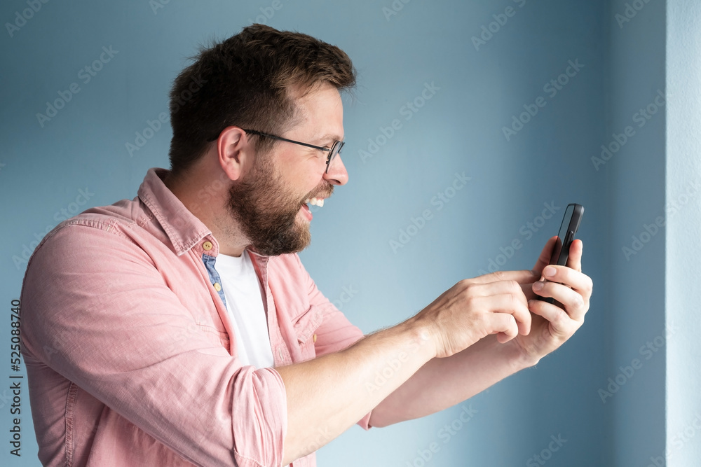 Profile of a joyful smiling man who holds a smartphone in his hands and communicates online via video communication. Profile of a joyful smiling man who holds a smartphone in his hands and communicates online via video communication.