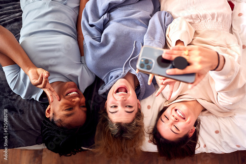 Overhead Shot Of Multi-Cultural Teenage Girl Friends Posing For Selfie On Mobile Phone At Home