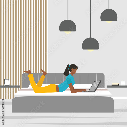 African american young woman lying in bed and using laptop at home