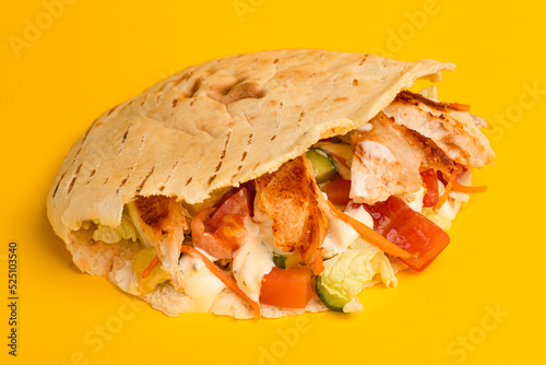 Shawarma in a pit with vegetables and chicken, side view yellow background