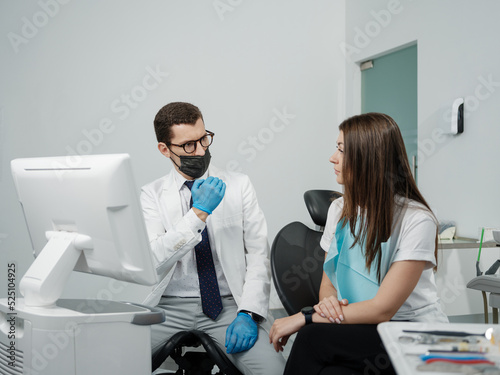 Male orthodontist with female patient looking on a screen during a medical consultation at the dental office