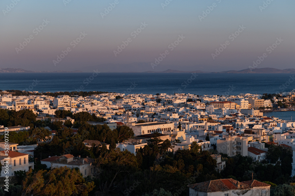 View on the city of Tinos from the hill during sunset. City centre and streets of village of Tinos with white Cycladic houses and Aegean Sea on background, Cyclades, Greece