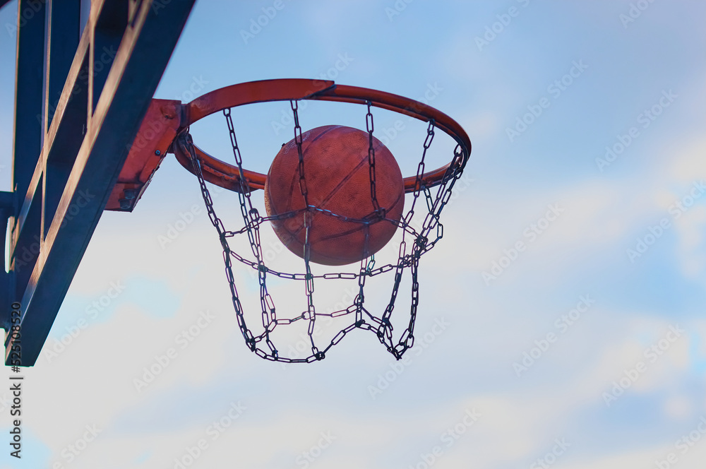 The ball flies into a basketball basket in a net of chains against the sky. Sports concept.