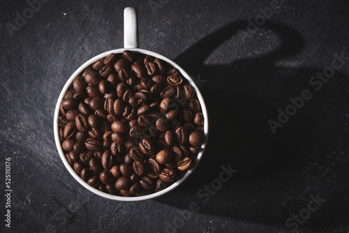 White cup of freshly brewed roasted coffee beans on gray background