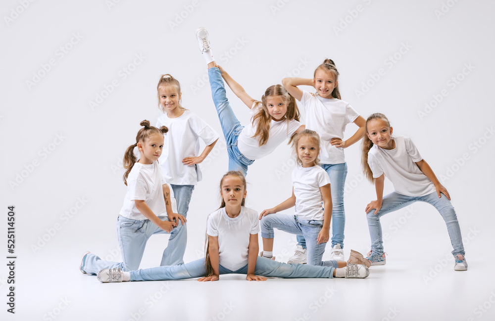 Obraz premium Portrait of happy, active little girls, sportive kids in casual clothes dancing isolated on white studio background. Concept of music, fashion, art, childhood, hobby