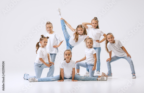 Portrait of happy, active little girls, sportive kids in casual clothes dancing isolated on white studio background. Concept of music, fashion, art, childhood, hobby