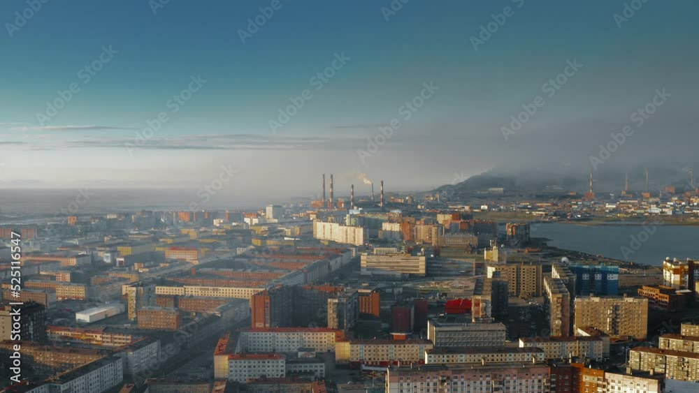 Multicolored houses, with industrial pipes at the back, from which steam or smoke comes out. Sunny hazy day. View from the drone. The copter is moving forward. 4K Multicolored houses, with industrial pipes at the back, from which steam or smoke comes out. Sunny hazy day. View from the drone. The copter is moving forward. 4K