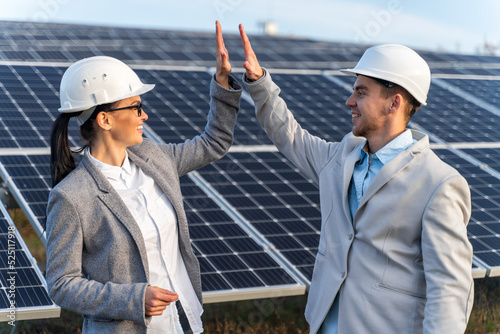 Happy moment of business colleagues in helmet standing in front of the energy panels in the outdoors