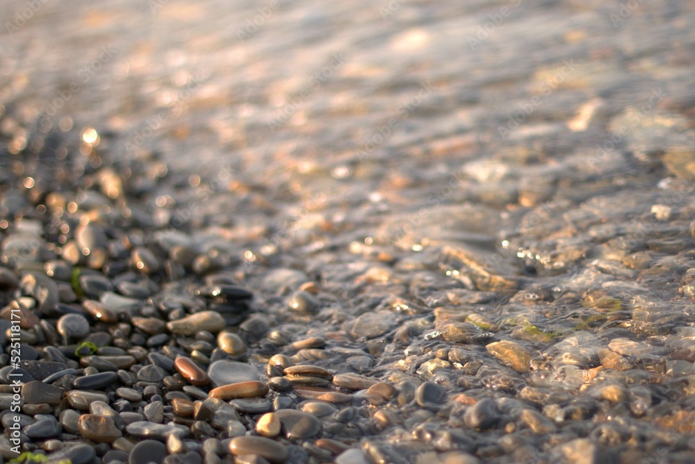 A transparent sea wave rolls over a rocky beach, the concept of rest and travel, calmness and reflection on a warm summer day, defocusing, blurred background, selective focus, bokeh. A transparent sea wave rolls over a rocky beach, the concept of rest and travel, calmness and reflection on a warm summer day, defocusing, blurred background, selective focus, bokeh.
