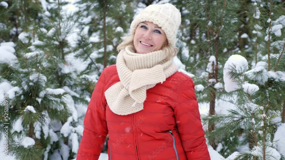 Middle-aged woman stands near snowy pine trees and smiles. Lady enjoys winter frosty weather in forest on nasty day closeup, slow motion Middle-aged woman stands near snowy pine trees and smiles. Lady enjoys winter frosty weather in forest on nasty day closeup, slow motion