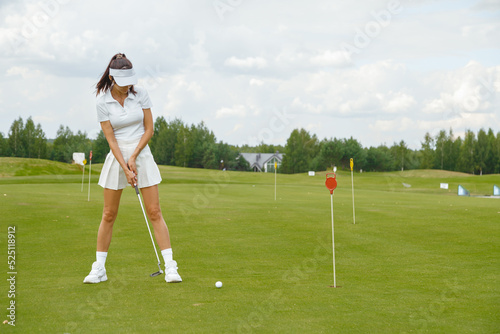 Woman in white short skirt practicing golf on the green