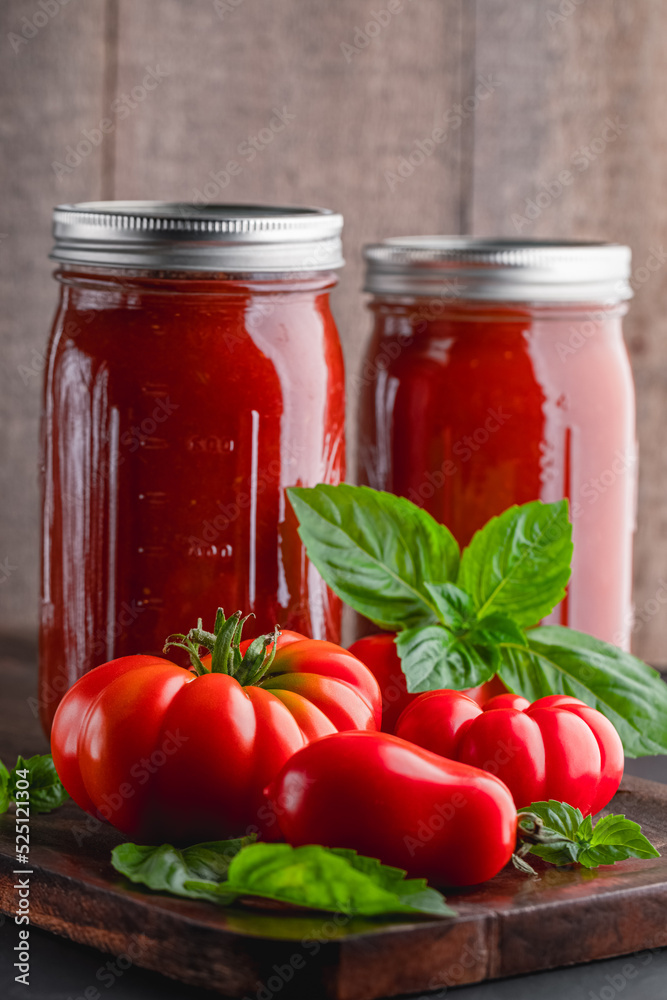 Fresh ripe, whole tomatoes, basil and home canned tomato sauce on a wooden cutting board Fresh ripe, whole tomatoes, basil and home canned tomato sauce on a wooden cutting board