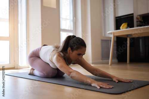 Side view portrait of a beautiful young woman in a white tank top doing yoga or pilates. Standing in one pose of a warrior. lessons at home. Arches the back