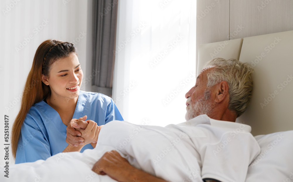 Obraz premium The young doctor held the hand of an old Caucasian man to take care of him. Talk to him from his illness lying in bed in his bedroom