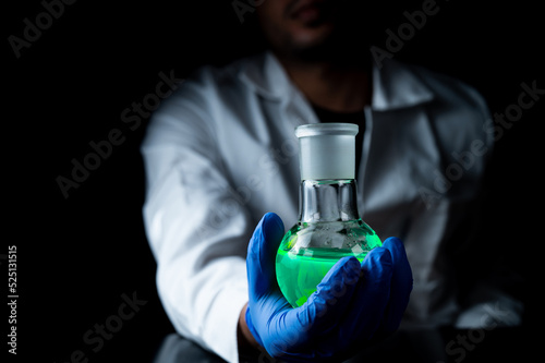 A woman scientist experimenting with a green fluorescent solution in a glass round bottom flask in dark chemistry laboratory