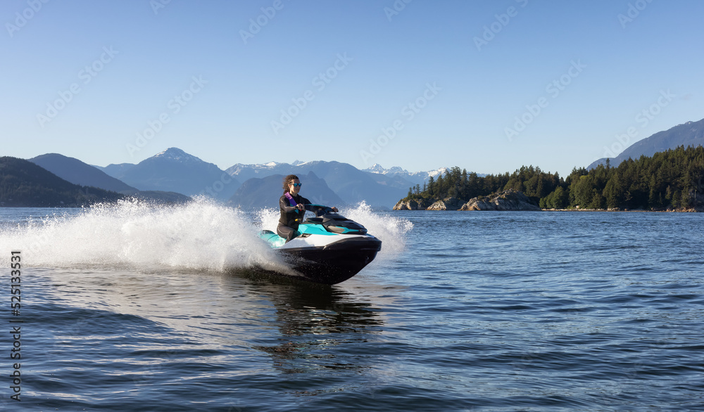 Fototapeta premium Adventurous Caucasian Woman on Water Scooter riding in the Ocean. Howe Sound and mountain landscape in background. West Vancouver, British Columbia, Canada.