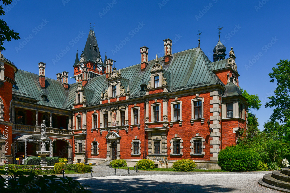 The Palace in Plawniowice, the palace and park complex from the 1980s. A magnificent building made of red brick with numerous decorations, the view on a sunny summer day.