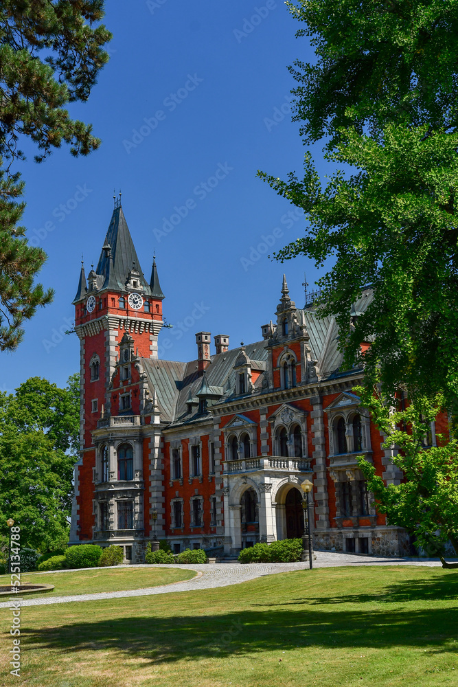 The Palace in Plawniowice, the palace and park complex from the 1980s. A magnificent building made of red brick with numerous decorations, the view on a sunny summer day.