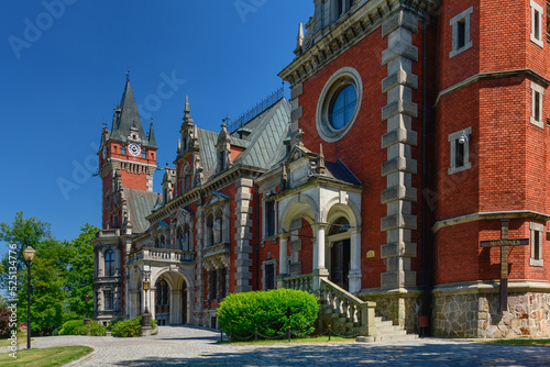 The Palace in Plawniowice, the palace and park complex from the 1980s. A magnificent building made of red brick with numerous decorations, the view on a sunny summer day.