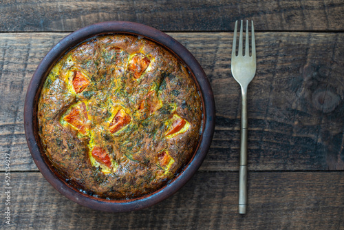 Ceramic bowl with vegetable frittata, simple vegetarian food, top view. Frittata with egg, tomato, pepper, onion, dill, parsley and cheese. Italian egg omelette