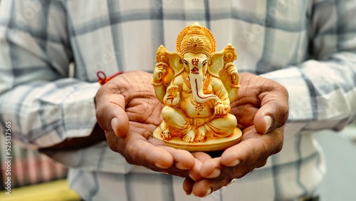 A Man holding Ganesha idol for Visarjan or Immersion in water annual ritual during Ganesh Chaturthi Hindu festival. Lord Ganapati idol in hands with sun rays background. Ganesh utsav in India photo