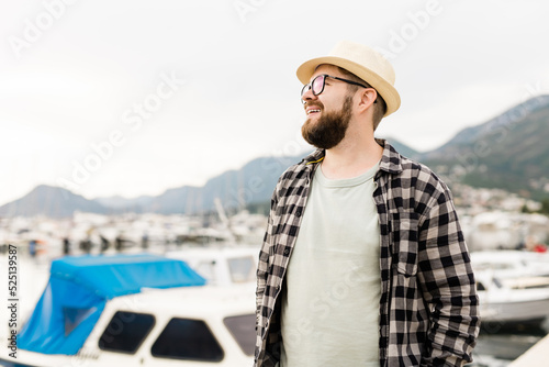 Handsome man wearing hat and glasses near marina with yachts. Portrait of laughing man with sea port background with copy space