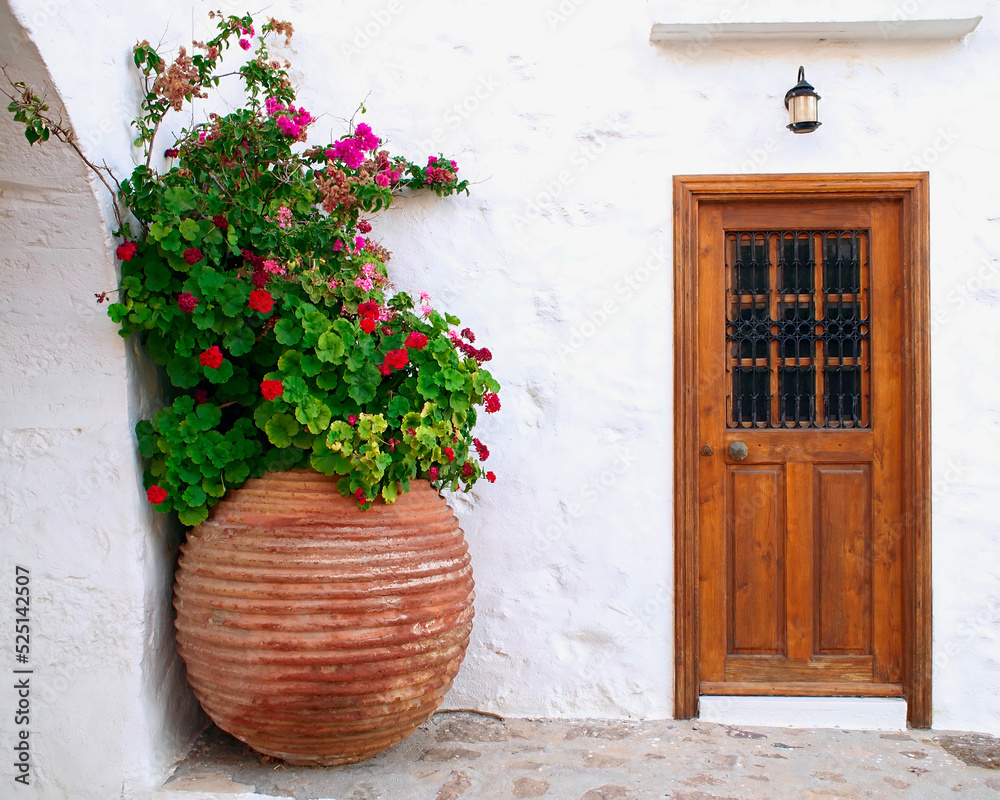 A white washed walls house with wooden door and huge flower jar. Milos island, Greece.