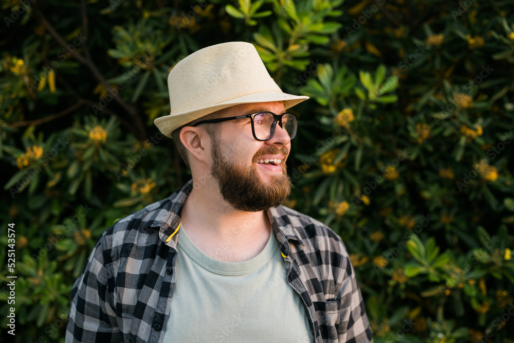 Laughing attractive man wearing hat over green tree background copy space and empty place for text - emotion and vacation travel holidays concept