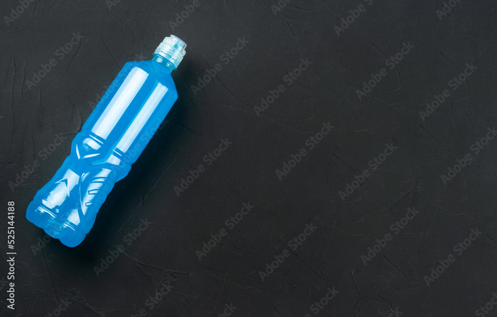 Naklejka premium Plastic bottle with blue isotonic drinks for sports on a dark concrete background, copy space