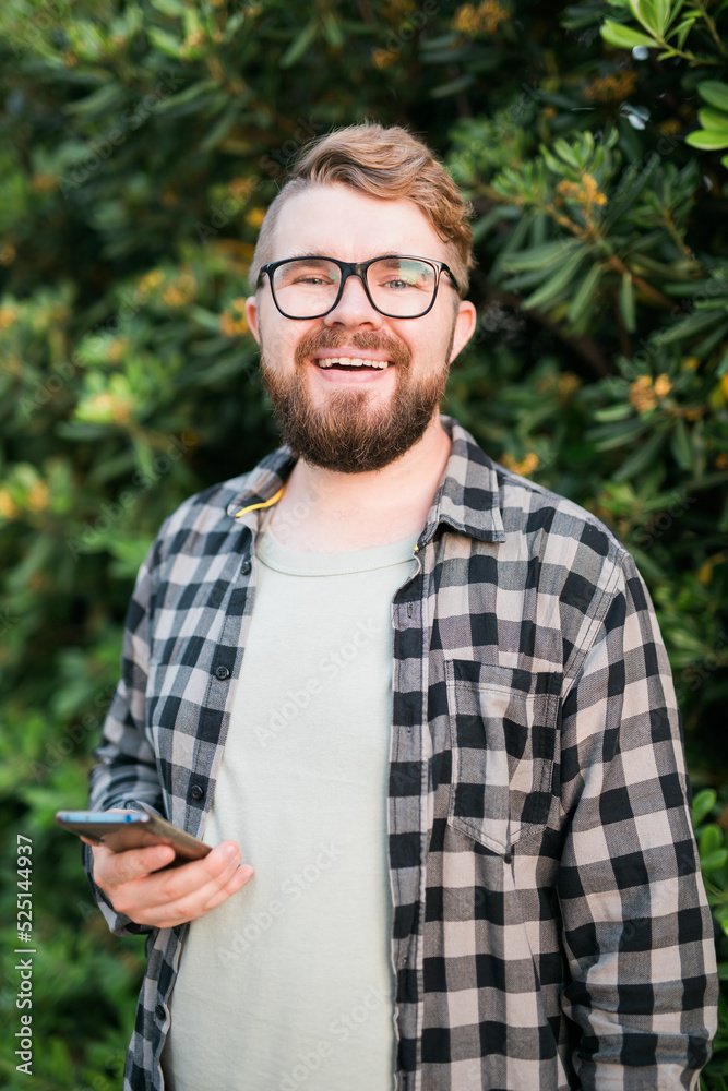 Fototapeta premium Portrait of attractive cheerful guy using smartphone for scrolling on social media over green tree background