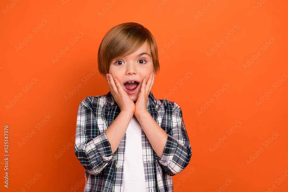 Photo of young boy hands touch cheeks astonished speechless novelty isolated over orange color background Photo of young boy hands touch cheeks astonished speechless novelty isolated over orange color background