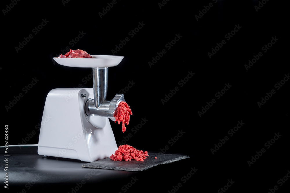 Meat grinder chopping red meat, on black background