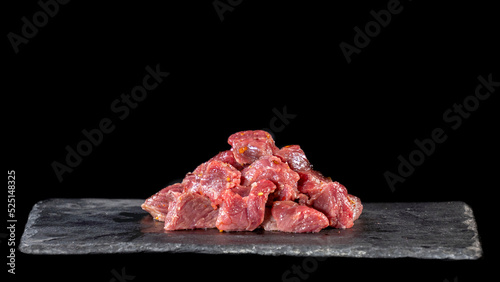 Raw beef, cubed and sprinkled with spices, on a slate and black background