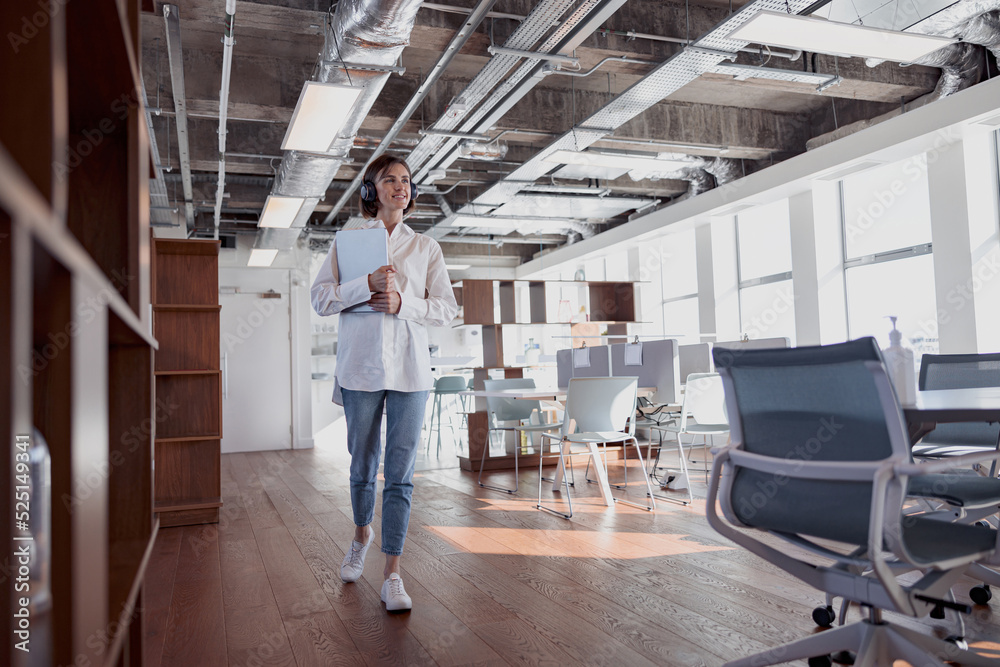 Attractive business woman in headphones with laptop crossing modern office. High quality photo Attractive business woman in headphones with laptop crossing modern office. High quality photo