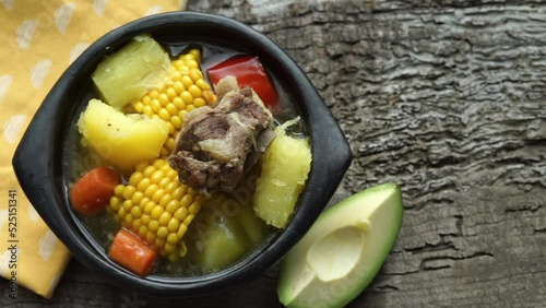 Sancocho dish on a wooden base. Hand placing avocado and spices.