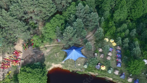 Aerial view of camping with kayaks on the beach of river on a sunny day. Nature background. Active rest concepts. Modern kayaks with paddles on beach near river. Summer camp activity.