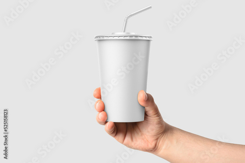 Paper soda cup in a hand with straw mockup template, isolated on light grey background. High resolution.