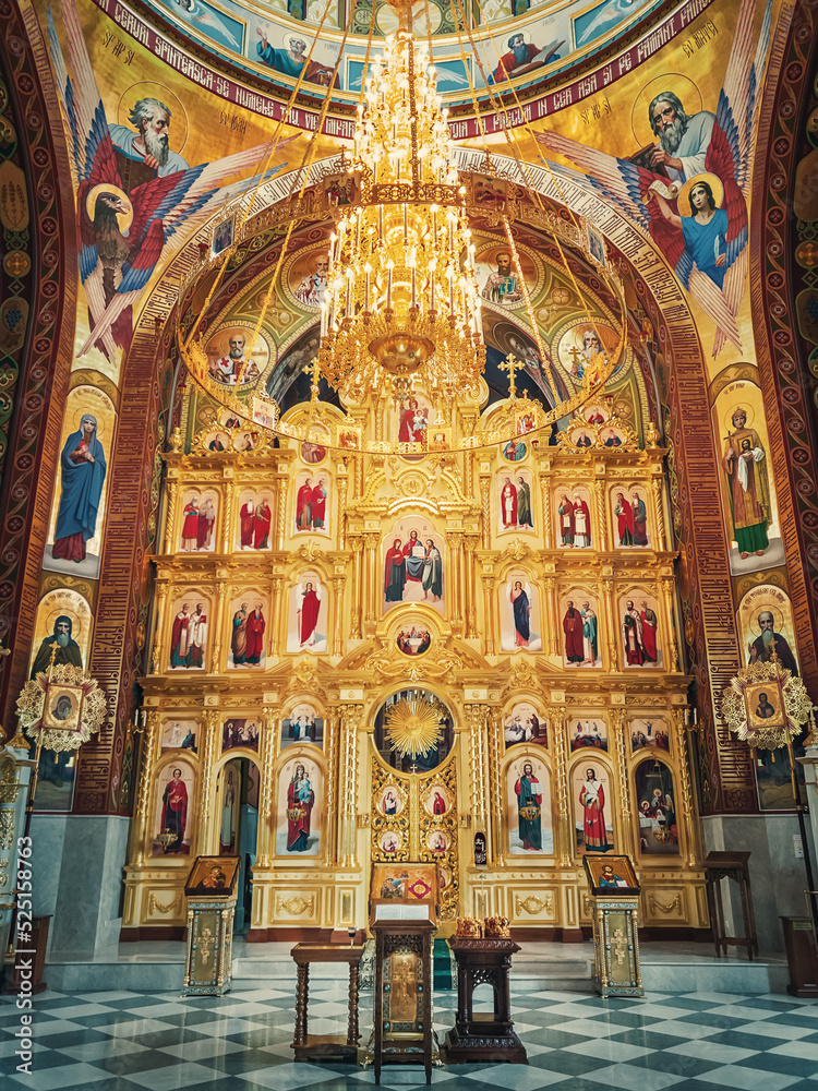 The altar and beautiful painted interior of the Curchi Monastery. Suspending golden chandelier with glowing lights. Different icons of saints as traditional for Christian Orthodox churches in Moldova