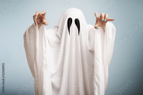 Halloween Concept. A white ghost with black eyes, made from a bedsheet on blue background photo
