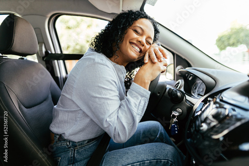 Fototapet Young and cheerful woman enjoying new car hugging steering wheel sitting inside