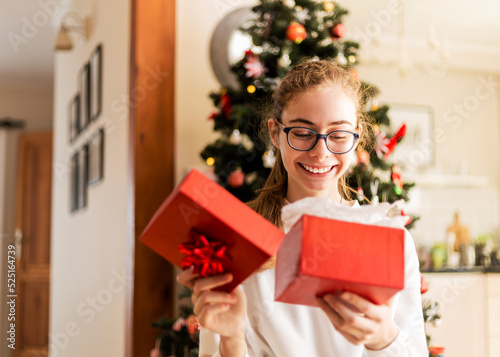 Christmas at family home - happy teenager girl opening red gift box (present)