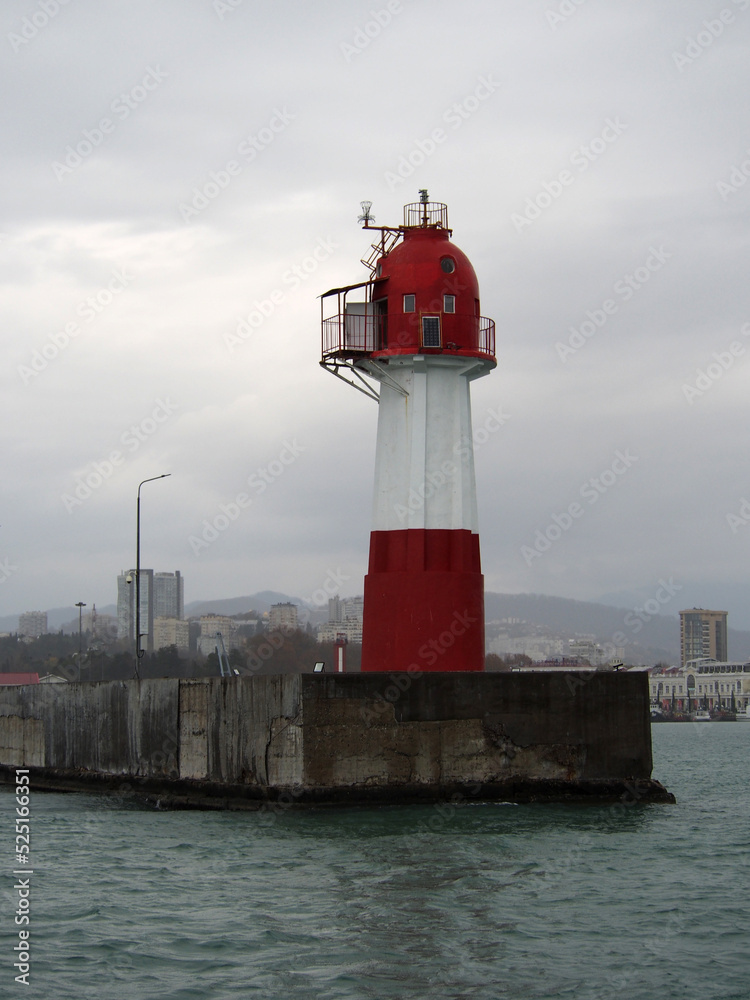 Lighthouse on the breakwater at the entrance to the port, against a gray, harsh winter sky. The concept of active recreation, sea travel.


