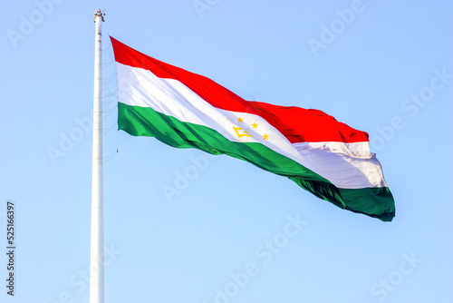 National red, white and green flag of Tajikistan on the flagpole against the blue sky.